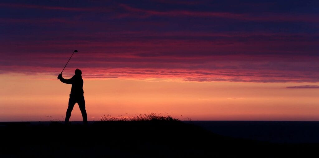 A Man Holding a Golf Club in Hand During Sunset